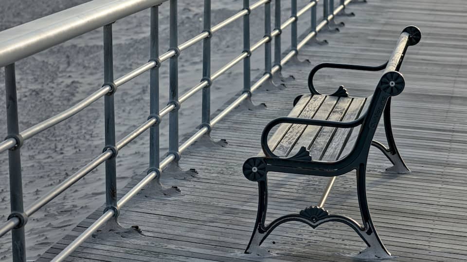 A wooden bench on a wooden boardwalk with metal railings.