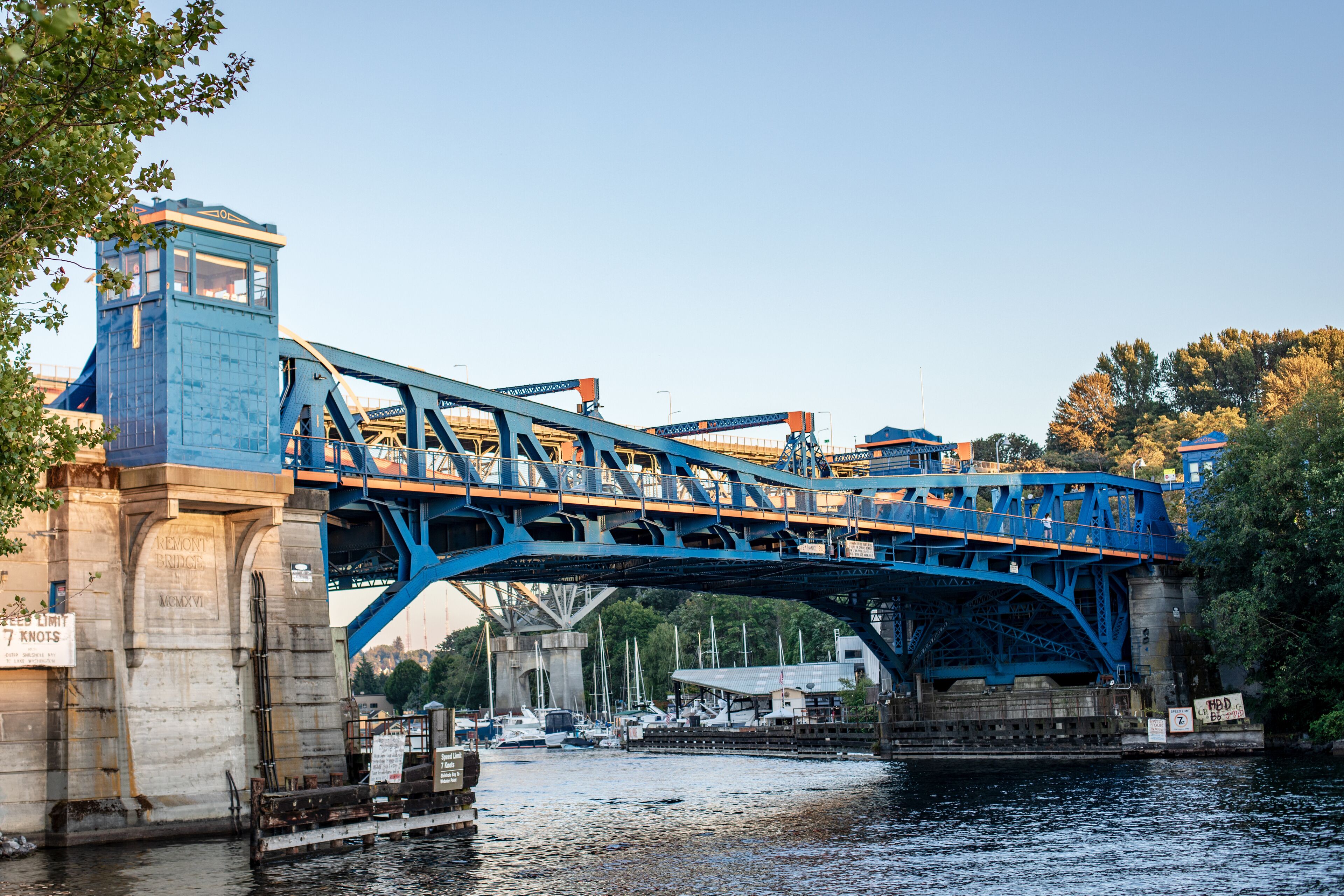 A blue bridge over a river with boats docked nearby.