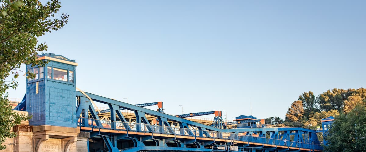 A blue bridge over a river with boats docked nearby.