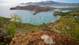 Una bahía costera con numerosos barcos, una playa arenosa y exuberante vegetación.