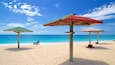 A beach with three wooden umbrellas and a clear blue sky.