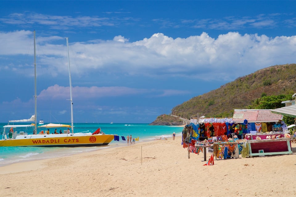 A beach with a yellow boat named 'WADADLI CATS' and a clothing stall.
