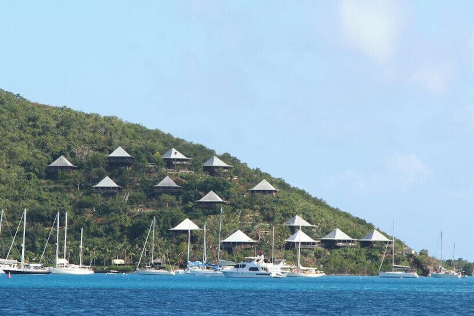 A coastal area with a row of beach huts on a hillside and several boats anchored in the water.
