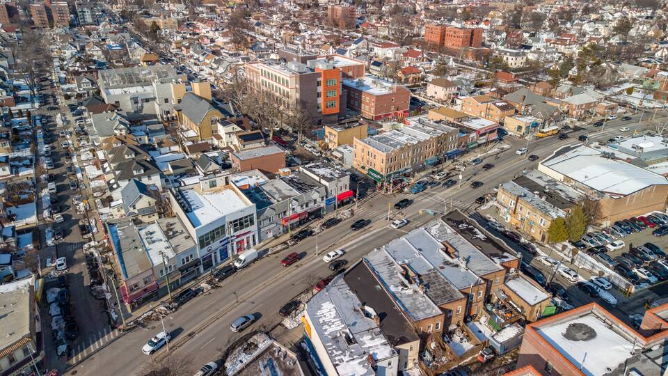 An aerial view of a densely packed urban area with a mix of residential and commercial buildings, a main street with vehicles, and a large red building with a distinctive shape.