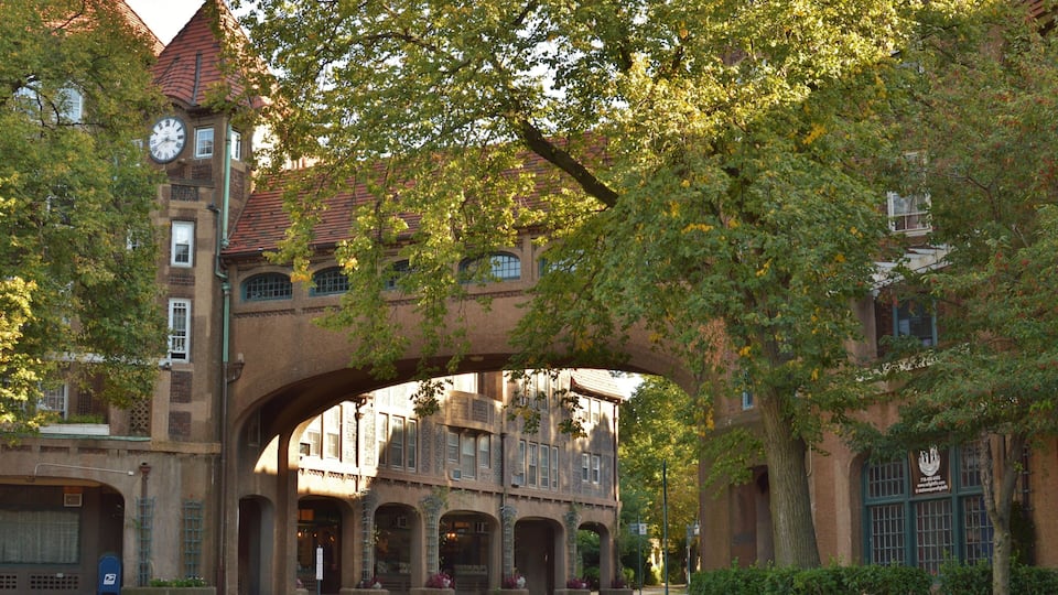 A historic building with a clock tower, arched entrance, and lush greenery.
