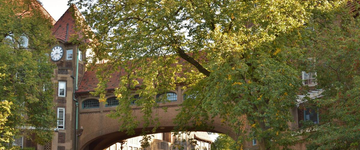A historic building with a clock tower, arched entrance, and lush greenery.