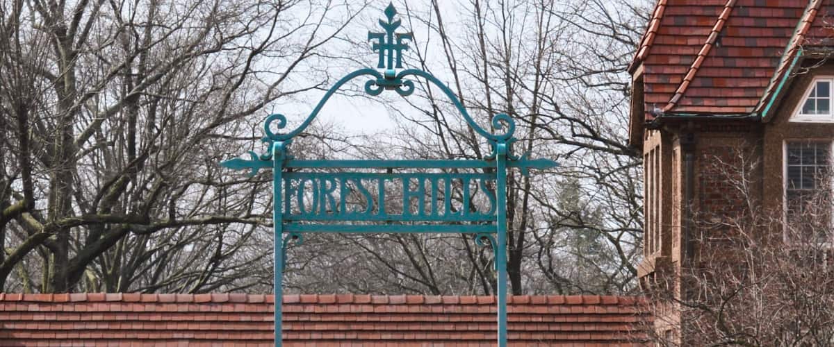 A wrought iron gate with 'FOREST HILLS' inscribed, a brick building, and leafless trees in the background.