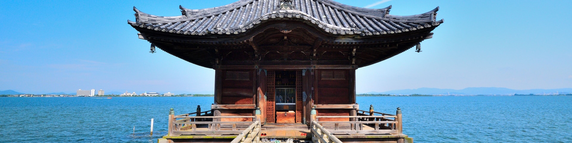 A traditional wooden pavilion on a pier extending into a calm body of water, with a clear blue sky above.