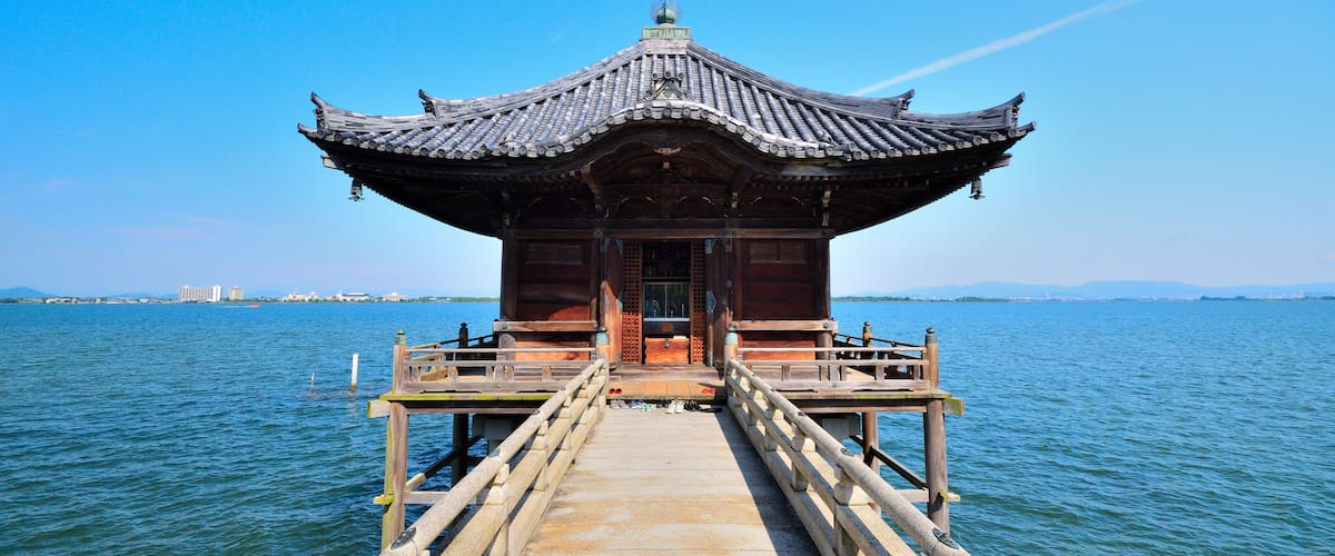 A traditional wooden pavilion on a pier extending into a calm body of water, with a clear blue sky above.