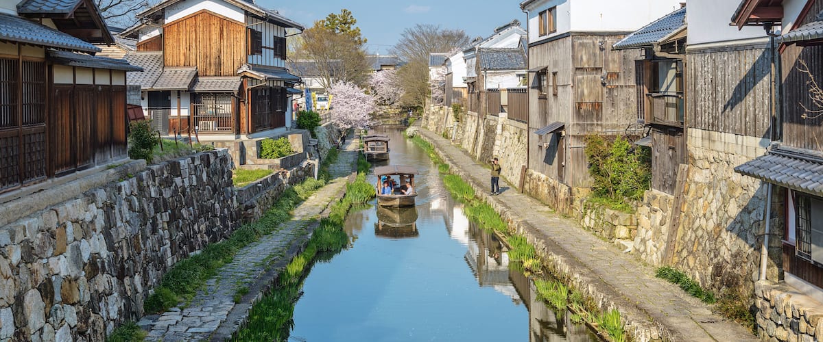 A narrow waterway flanked by traditional wooden houses with stone walls and a boat in the distance.