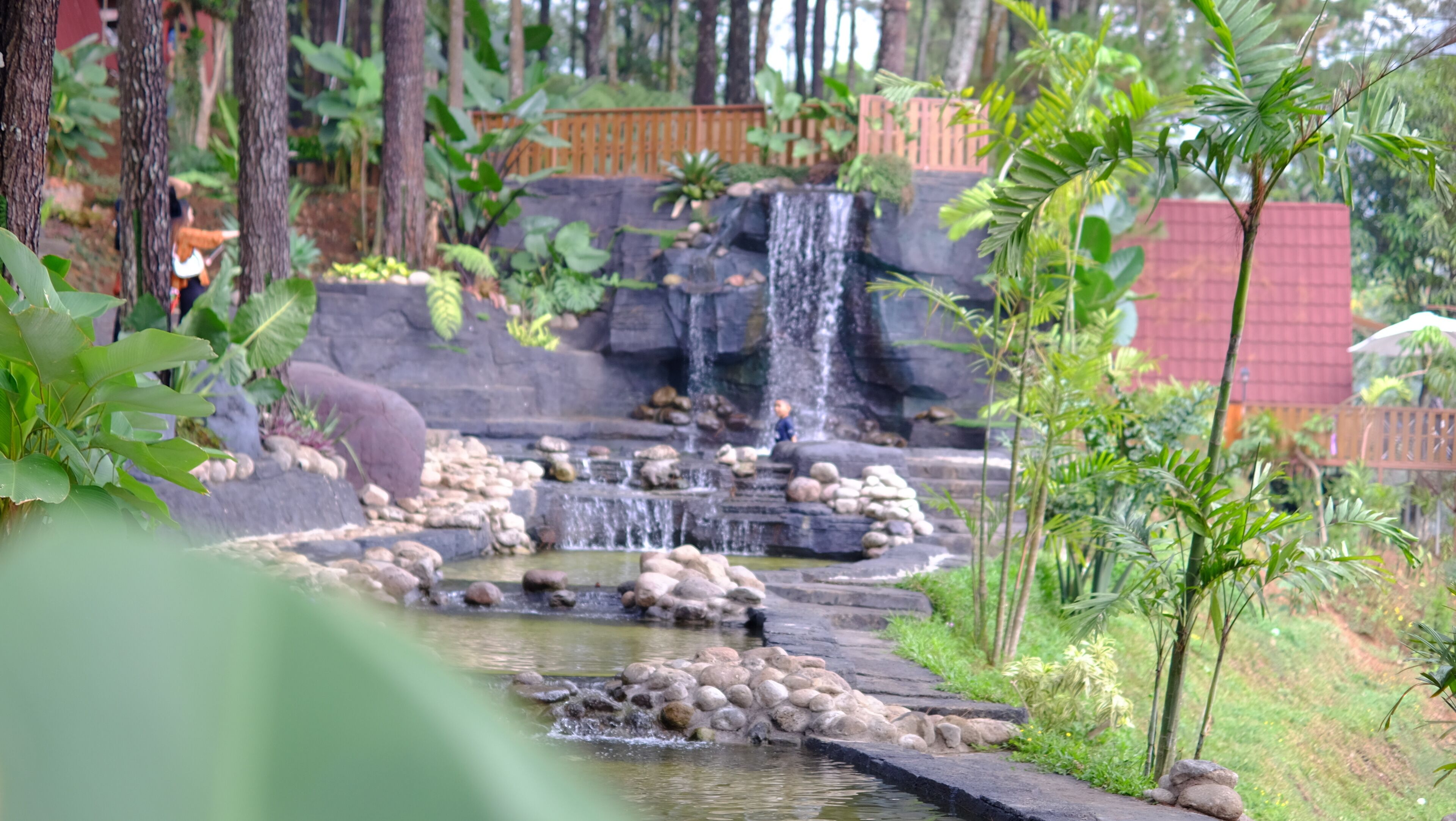 A waterfall cascading over rocks into a pond surrounded by lush greenery and trees.