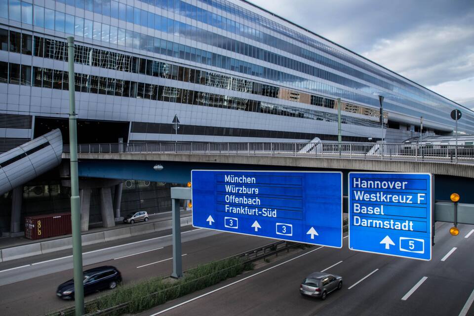Ein modernes Gebäude mit Glasfassade und einem Straßenschild, das Wegweiser zu verschiedenen Städten zeigt.