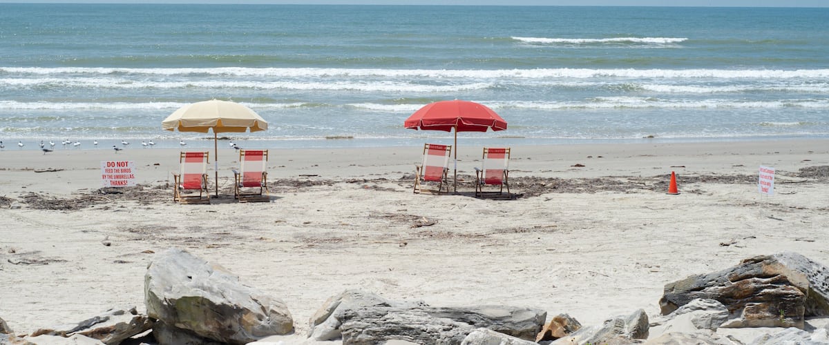 A beach with red and white beach chairs, umbrellas, and warning signs.