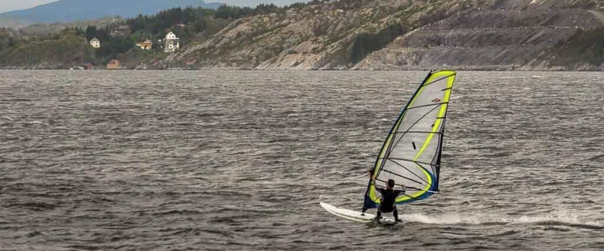 A person windsurfing on a lake with a mountainous backdrop.
