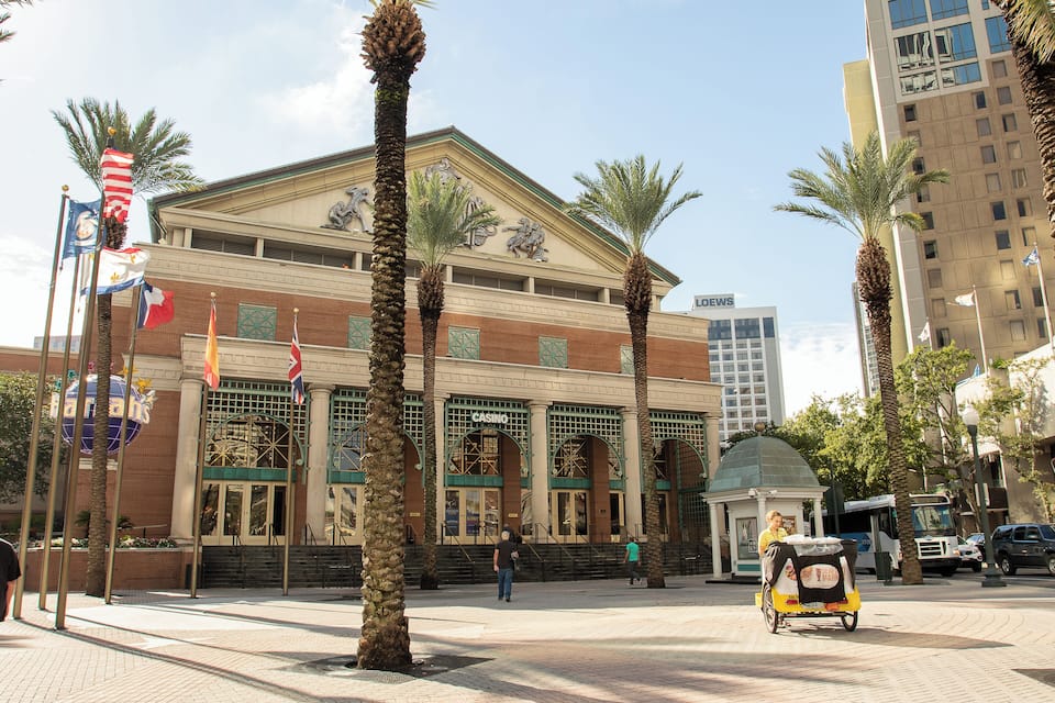 A casino building with palm trees, flags, and a bus in the background.