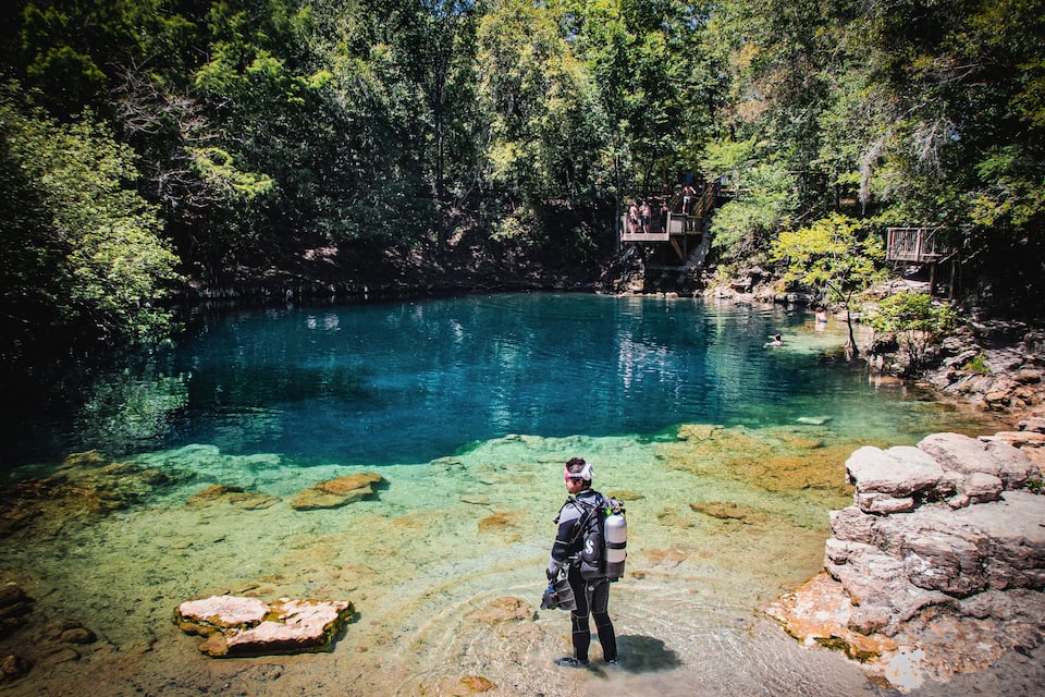 A diver in a forested area with a clear blue lake.