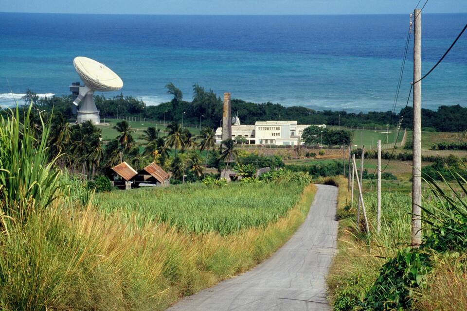 A coastal road with a satellite dish, a white building, and palm trees.
