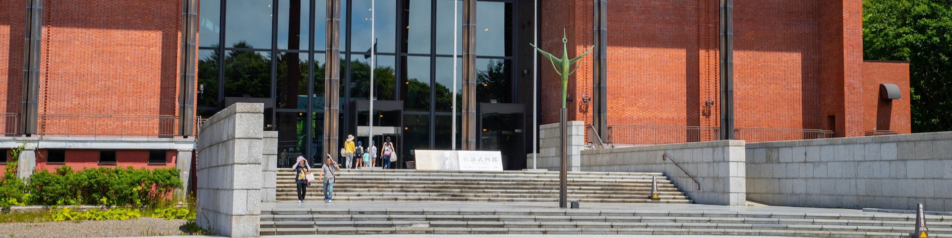 A modern building with large glass windows, a brick facade, and a flagpole with flags.
