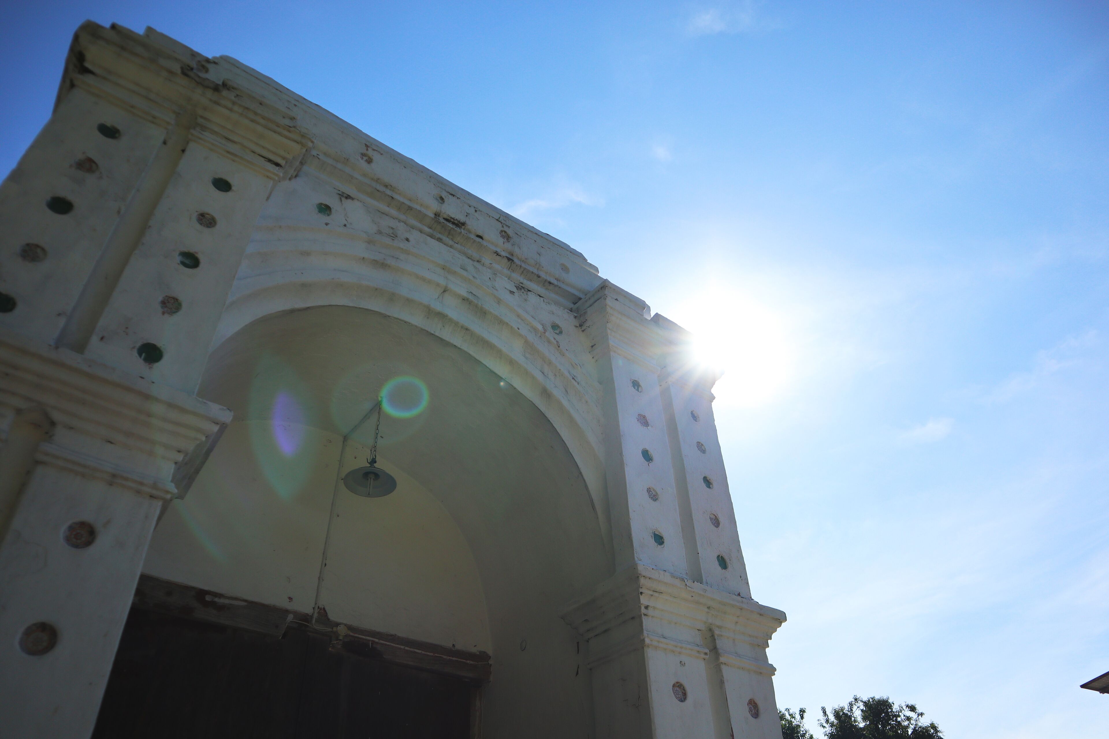 An arched architectural structure with circular windows and a sun shining through it.