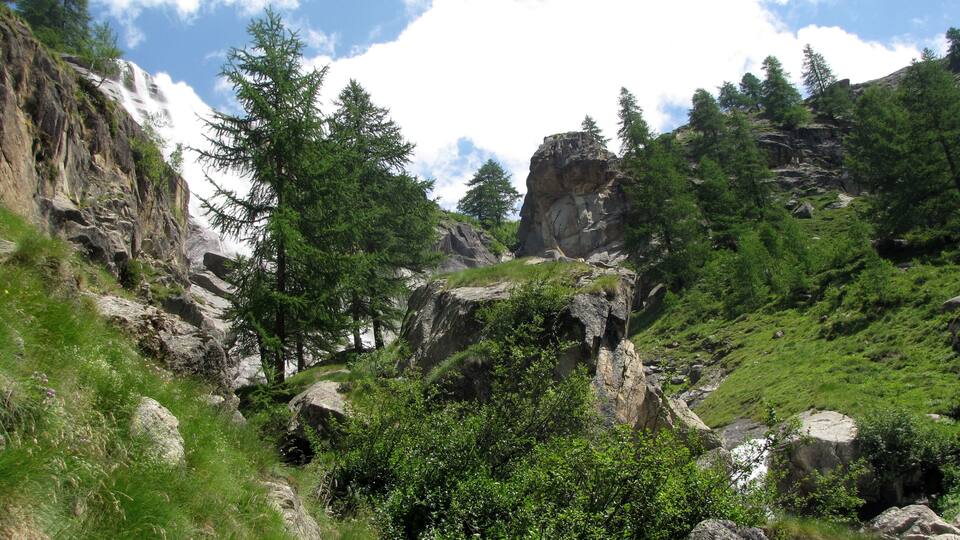 A mountainous landscape with a waterfall, rocky outcrops, and dense green vegetation.