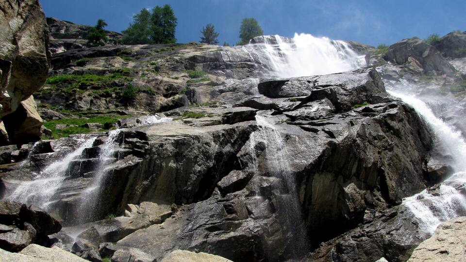 A multi-tiered waterfall cascading over rocky terrain with sparse vegetation.