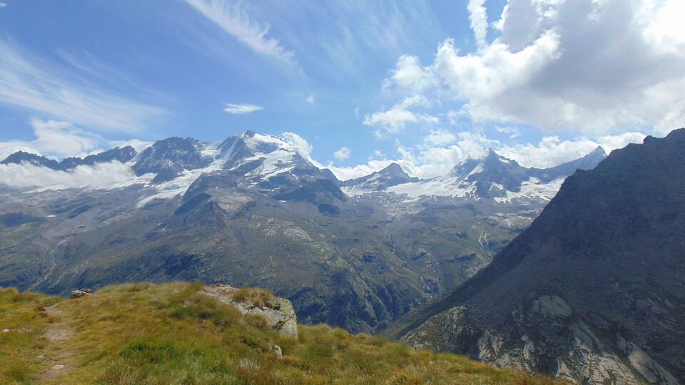 A mountain landscape with a clear sky and a path leading towards the peaks.