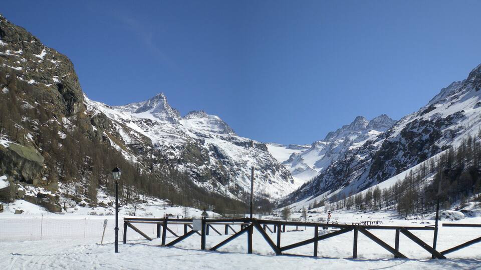 A snow-covered mountain pass with a wooden fence and a lamppost.