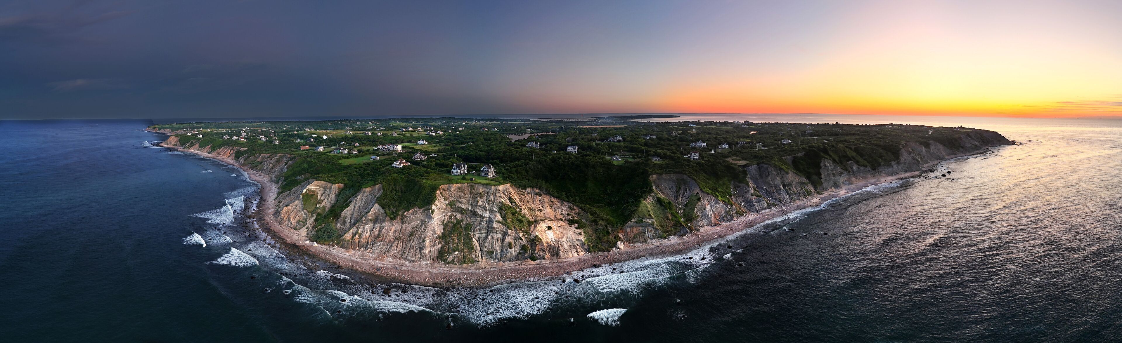 Aerial view of dramatic cliffs meet the dark, churning sea under a sky ablaze with the fiery hues of sunset, New Shoreham, Rhode Island, United States.