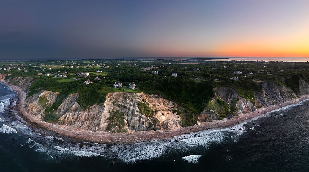 Aerial view of dramatic cliffs meet the dark, churning sea under a sky ablaze with the fiery hues of sunset, New Shoreham, Rhode Island, United States.