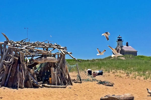 Une plage de sable avec une structure en bois, un phare et des mouettes qui volent.