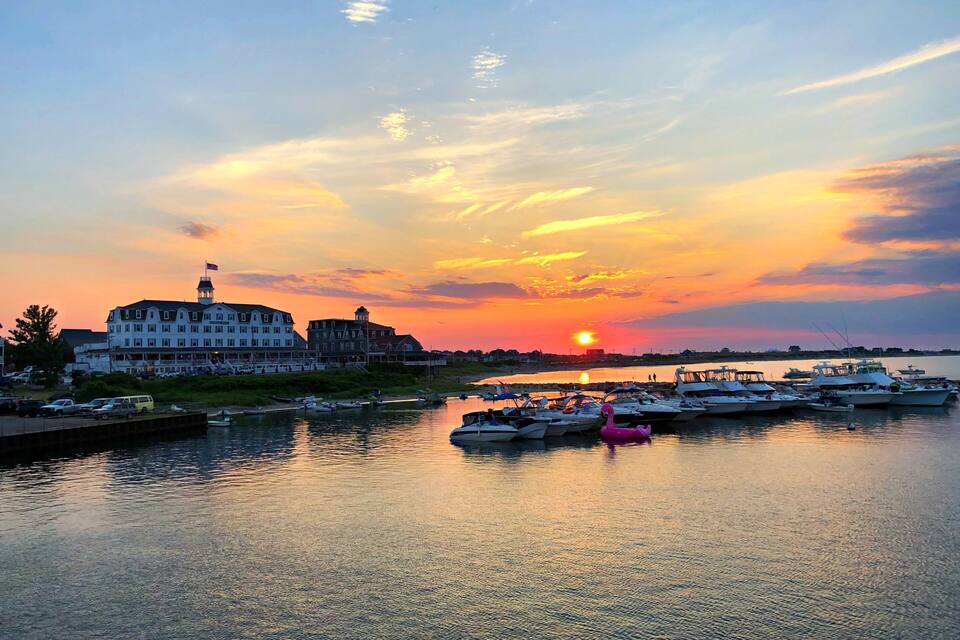 A marina at sunset with boats docked, a prominent white building with a flag, and a pink flamingo float.
