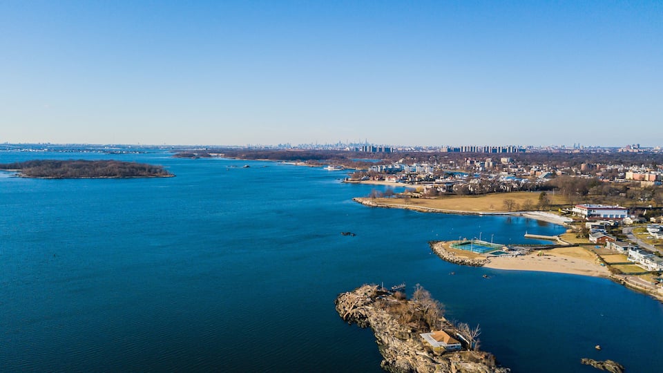 A river with a cityscape in the background, a small island, and a rocky outcrop in the foreground.