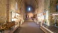 Un ancien couloir en pierre où sont exposés des objets d’art historiques et où se trouve une grande sculpture en pierre.