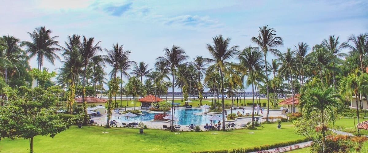 A resort with a swimming pool, palm trees, and a well-maintained lawn.