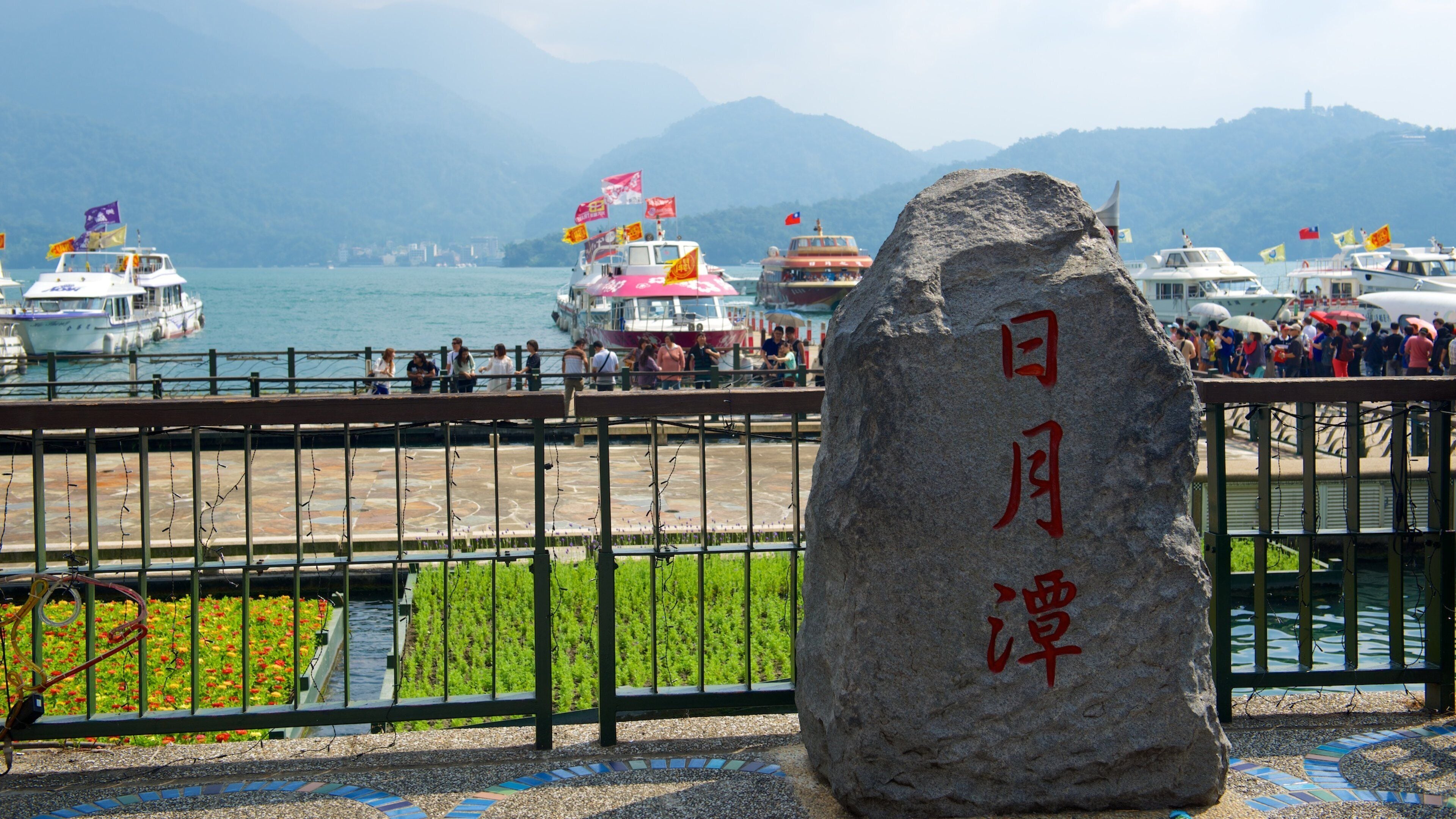 A stone with Chinese characters, a waterfront with boats, and a mountainous backdrop.