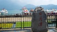 A stone with Chinese characters, a waterfront with boats, and a mountainous backdrop.