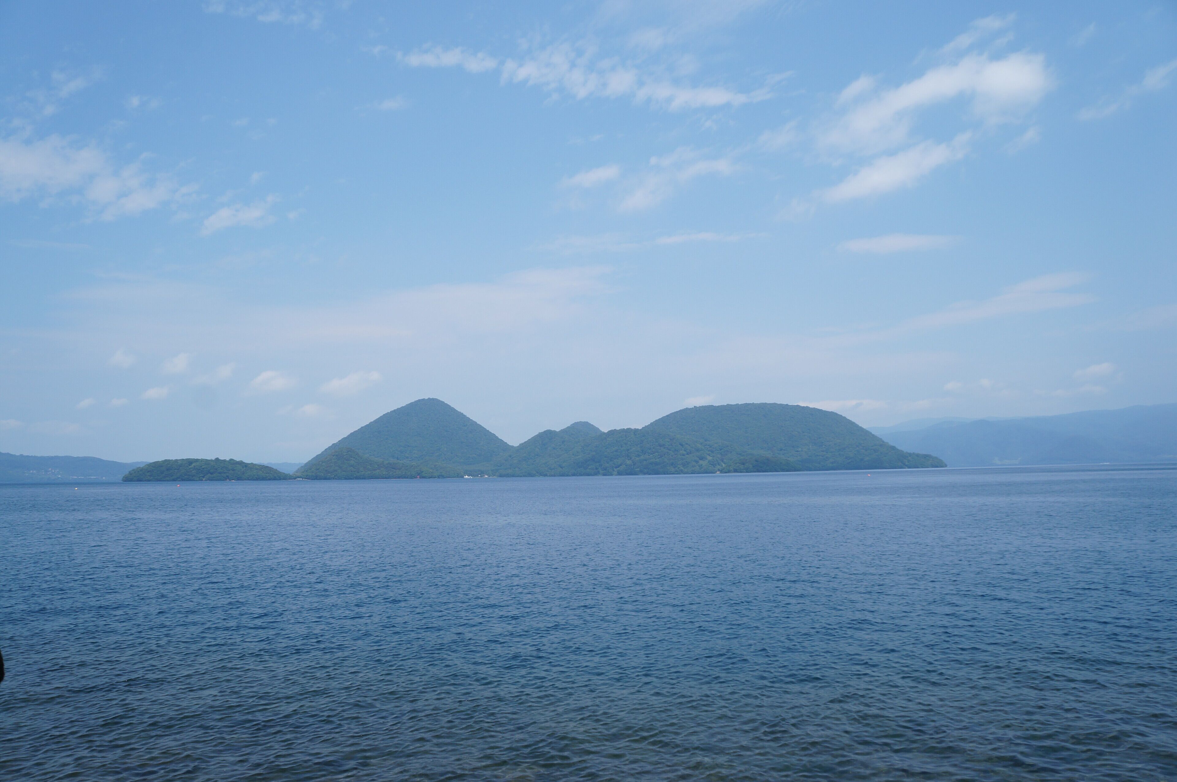 A calm lake with two green islands in the distance under a clear sky.