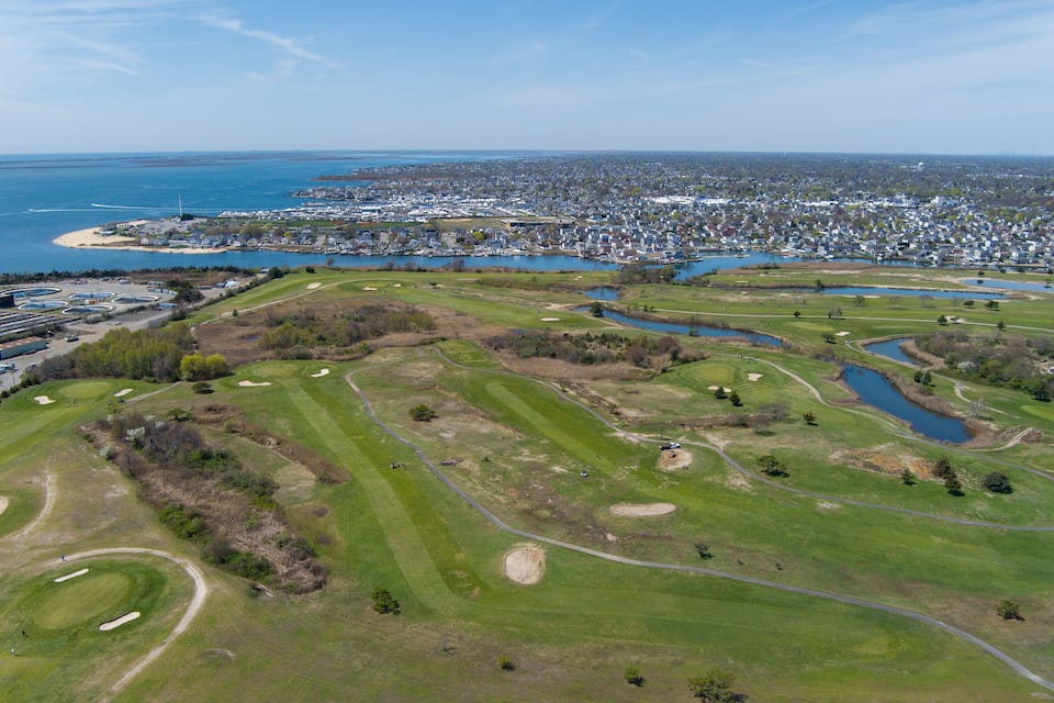 Ein Luftbild eines Golfplatzes mit einer Küstenstadt im Hintergrund.