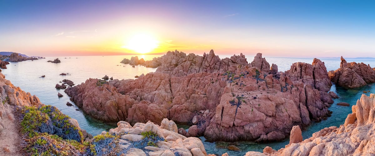 A coastal landscape with rocky formations and clear blue waters during sunset.