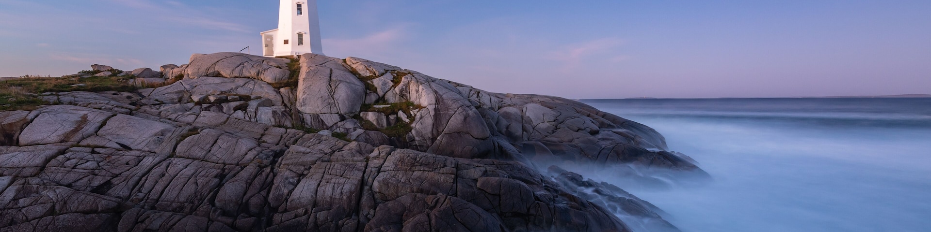 Un faro en un promontorio rocoso con un mar en primer plano, capturado con exposición prolongada.