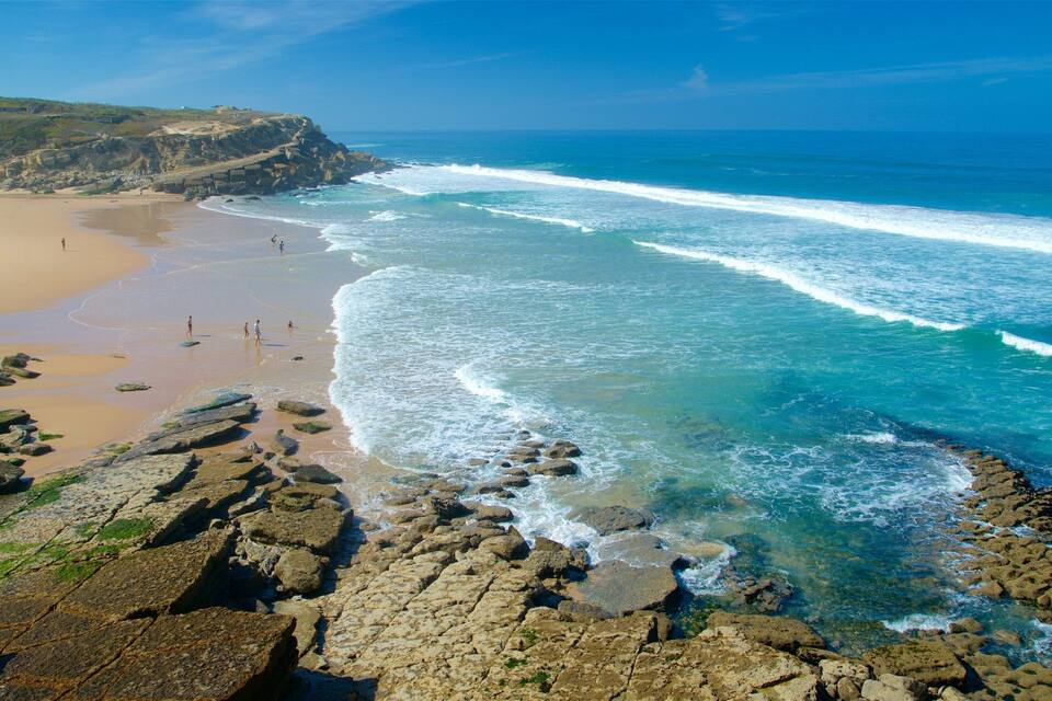 Paisaje costero con playa arenosa, costa rocosa y olas azules claras.