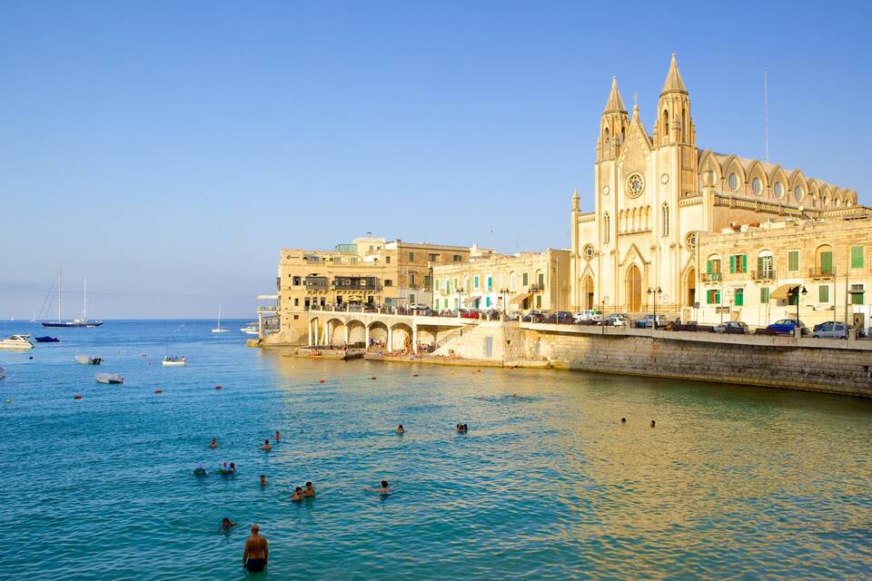 Un pueblo costero con una iglesia destacada, un puente de piedra y barcos en el agua.
