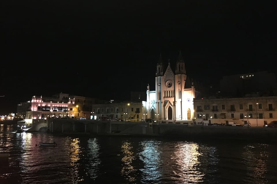 Vista nocturna de una ciudad con una iglesia iluminada destacada y un puente sobre el agua.