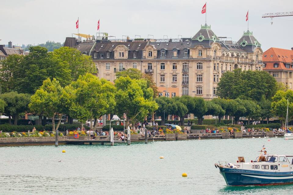 A river with boats, a row of trees, and historic buildings in the background.