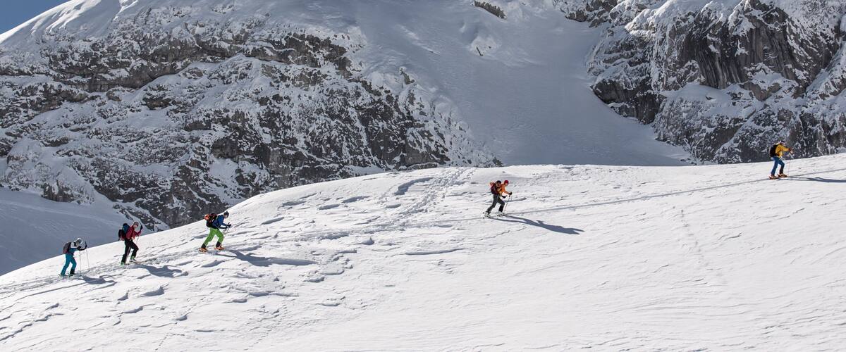 A snowy mountain landscape with climbers ascending a slope.