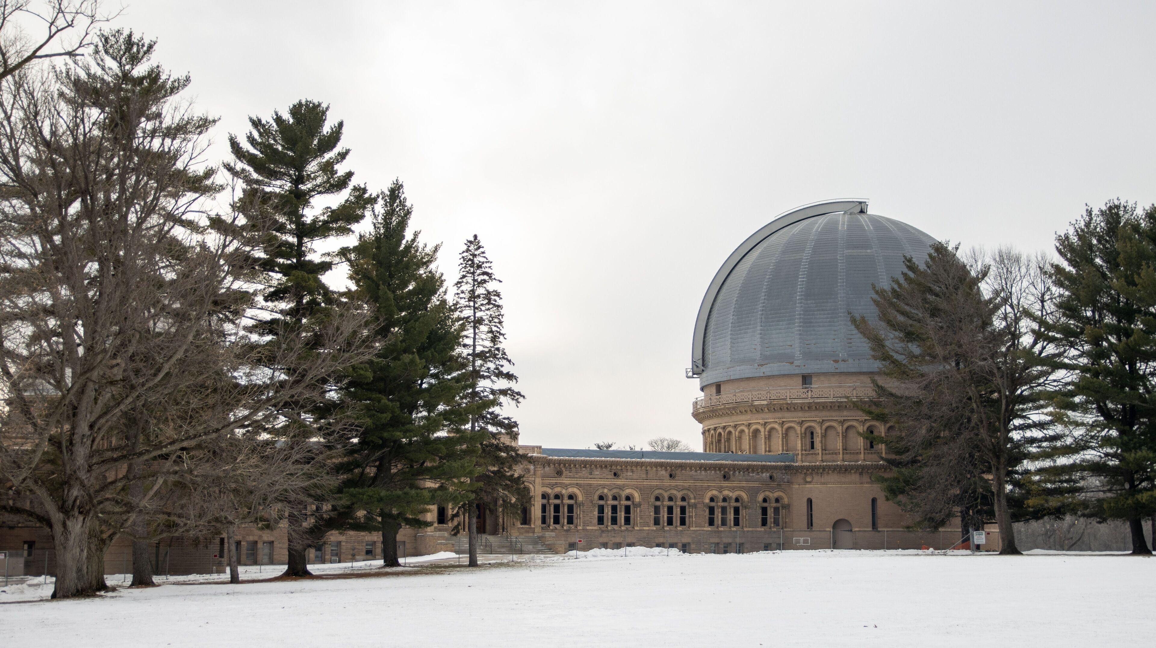 A large building with a dome and arched windows, surrounded by snow and trees.