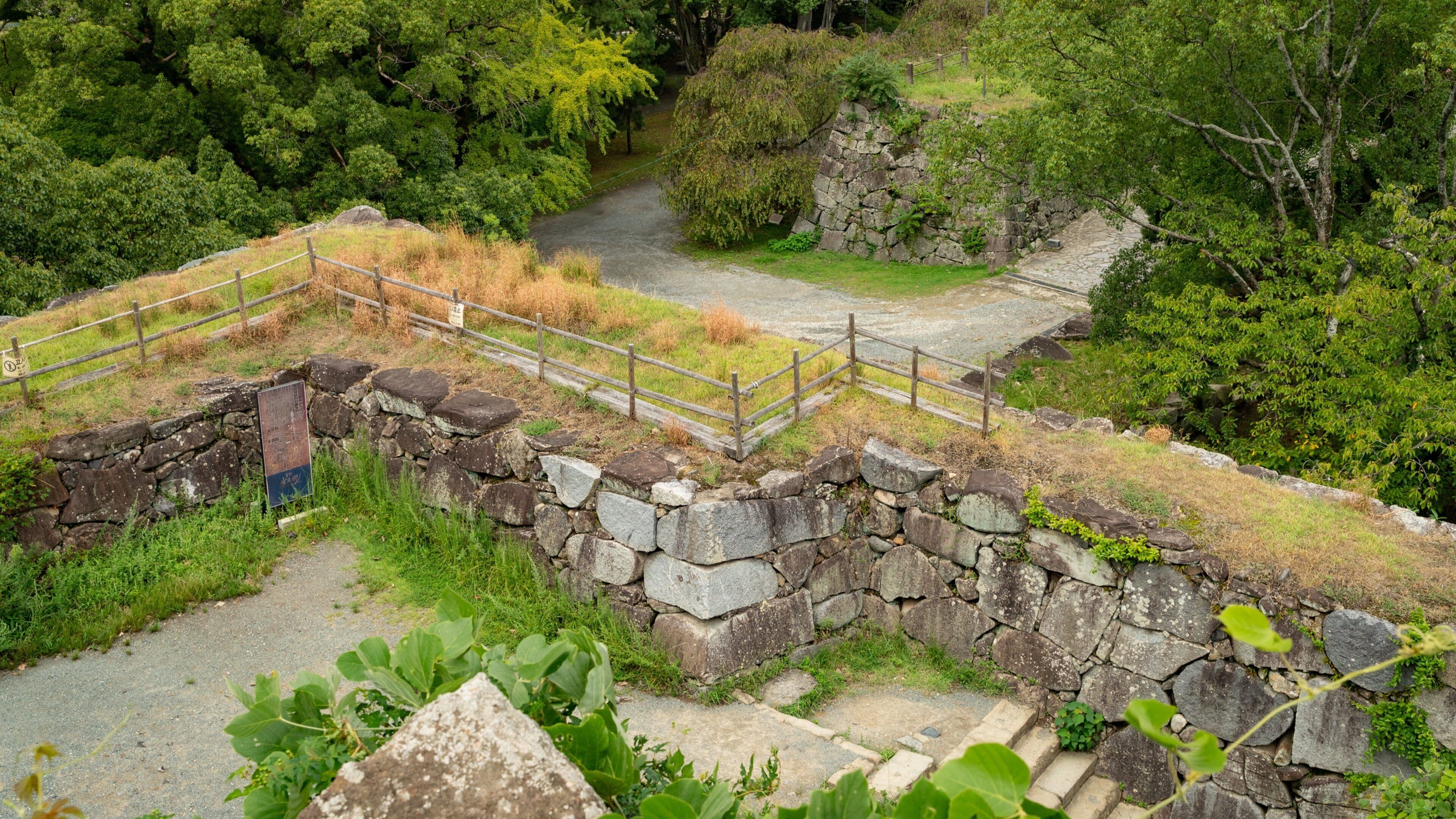 A stone wall with a wooden fence, surrounded by greenery and trees.