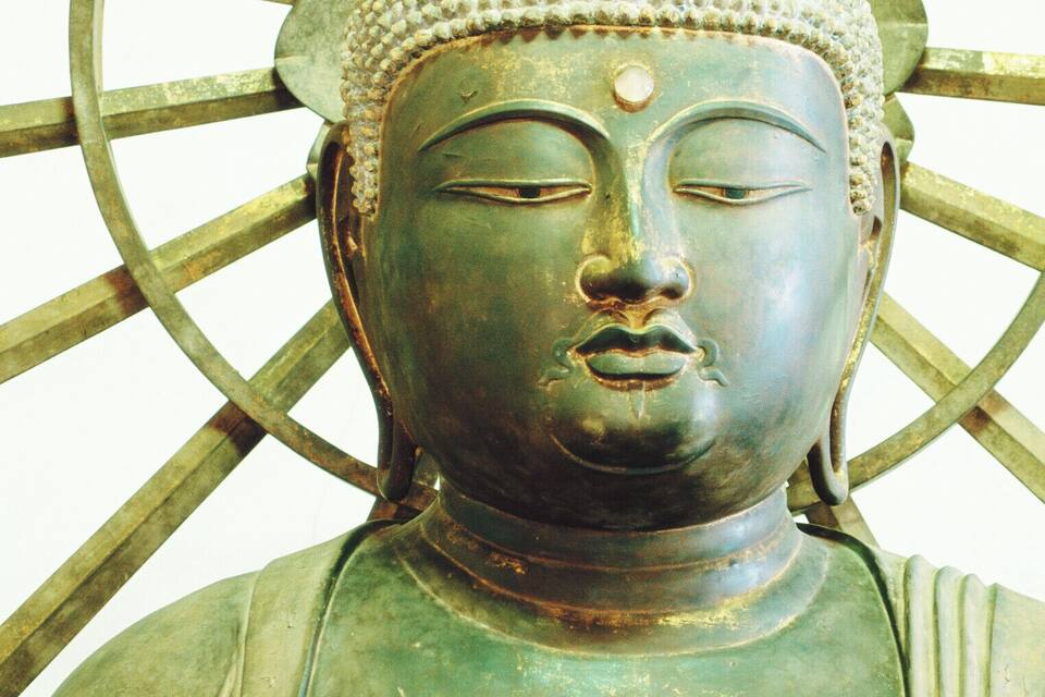 A statue with a greenish patina, a white headdress, and a large circular halo.