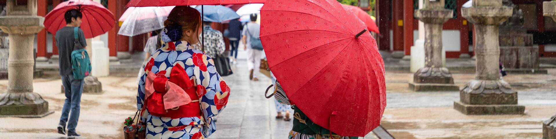 Un templo japonés tradicional con sombrillas rojas sostenidas por visitantes.