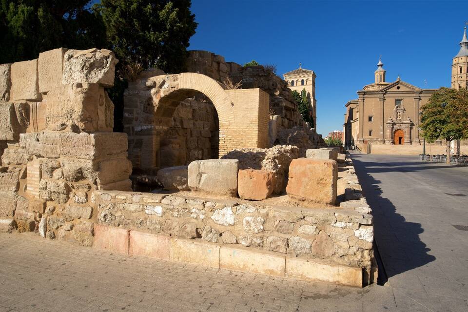 Ancient ruins with a large archway, a church with a bell tower, and a clear blue sky.